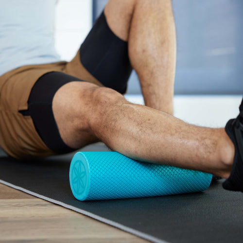 Up close of persons leg on yoga mat with the Restore Compact Foam Roller under the calf